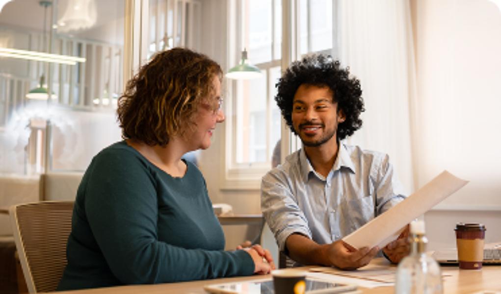 Two professionals seated next to each other in a modern office, one holding a document, discuss strategic partner alignment and collaborative growth.