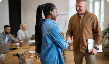 Two colleagues shake hands in a bright, modern office to represent partnership alignment and relationship building.