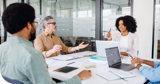 A businesswoman smiles over her laptop as she tells a compelling story to her coworkers about performance alignment and partner marketing.